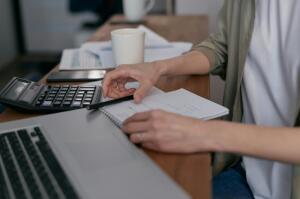 Person creates their budget using paper, laptop, and a calculator